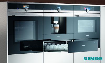 Siemens: Vernetzte Einbaubacköfen der Serie iQ 700 Siemens glassdraftAir Dunstabzug hinter Kochfeld mit aufsteigendem Dampf, moderne offene Küche, Frau im Hintergrund.